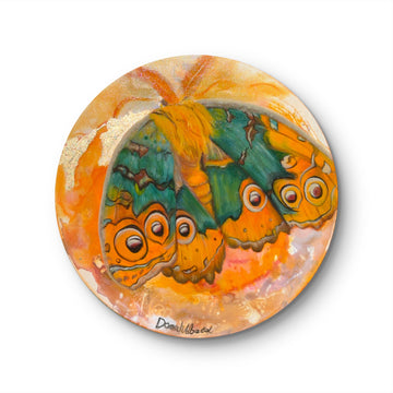 A vibrant painting depicting a moth with rich hues of turquoise, amber, and gold, with intricate details and metallic accents on a round canvas.