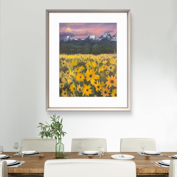 Framed artwork of a sunflower field with mountains on a wall above a dining table.